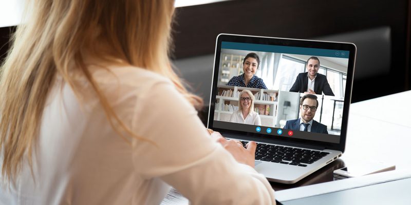 Back view of businesswoman speak using Webcam conference on laptop with diverse colleagues, female employee talk on video call with multiracial coworkers engaged in online briefing from home