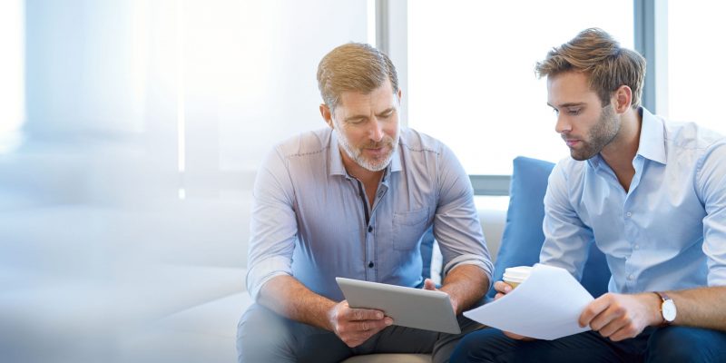 Mature businessman using a digital tablet to discuss information with a younger colleague in a modern business lounge